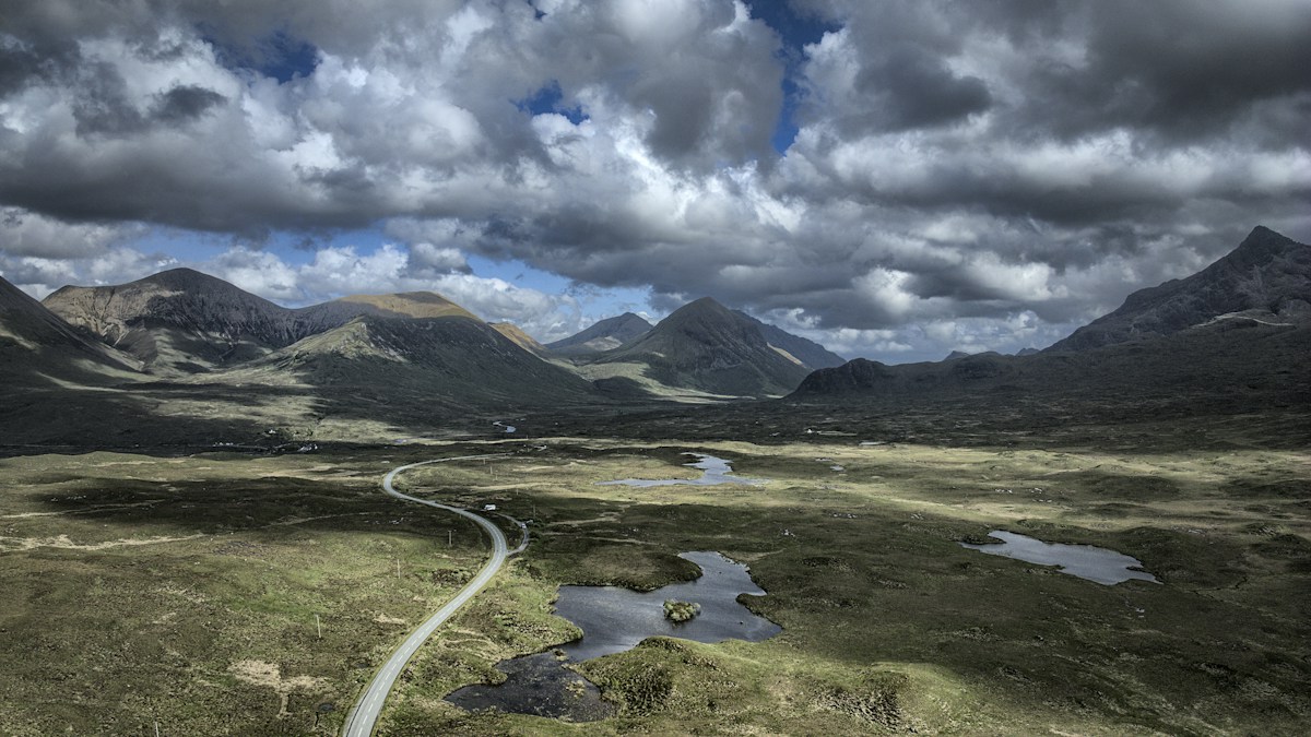 Mountains and winding road under a dramatic sky.