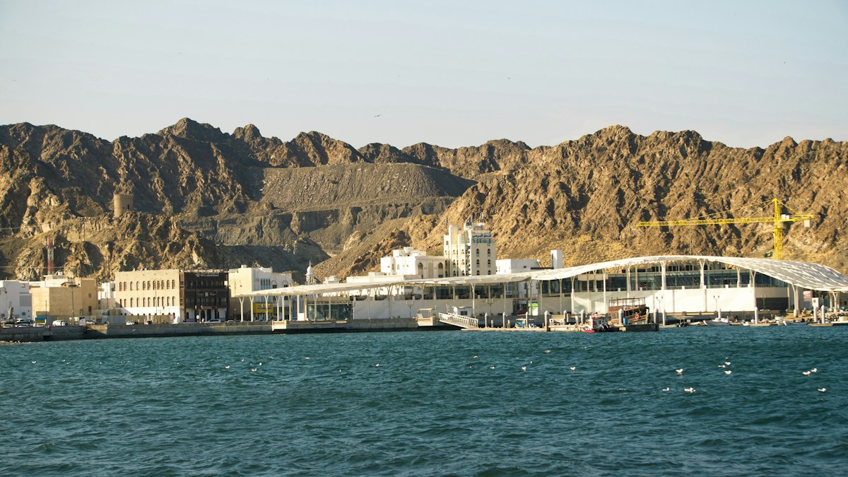 Modern buildings stand by the sea with mountain backdrop.