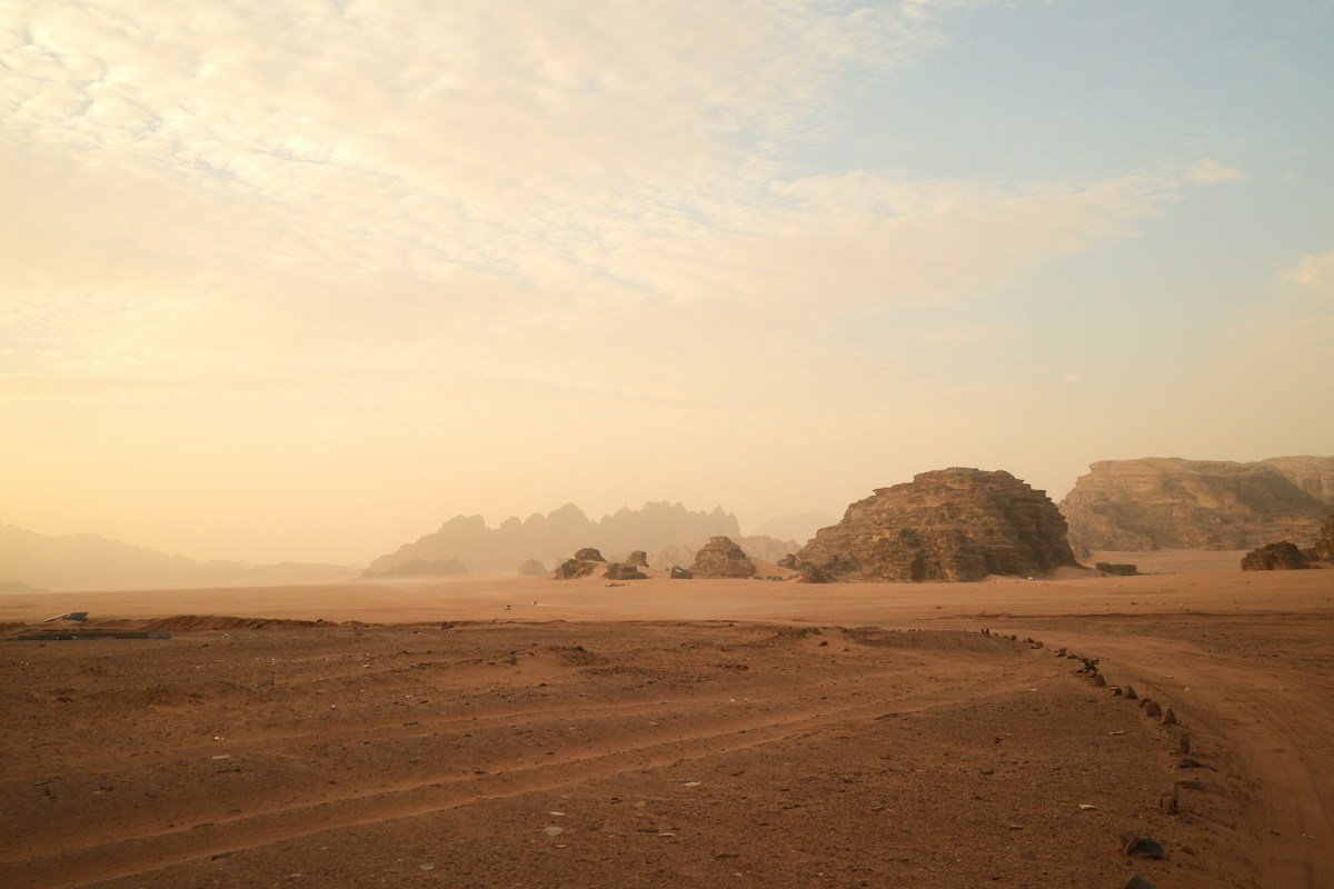 Sandy desert landscape with rock formations at sunrise.